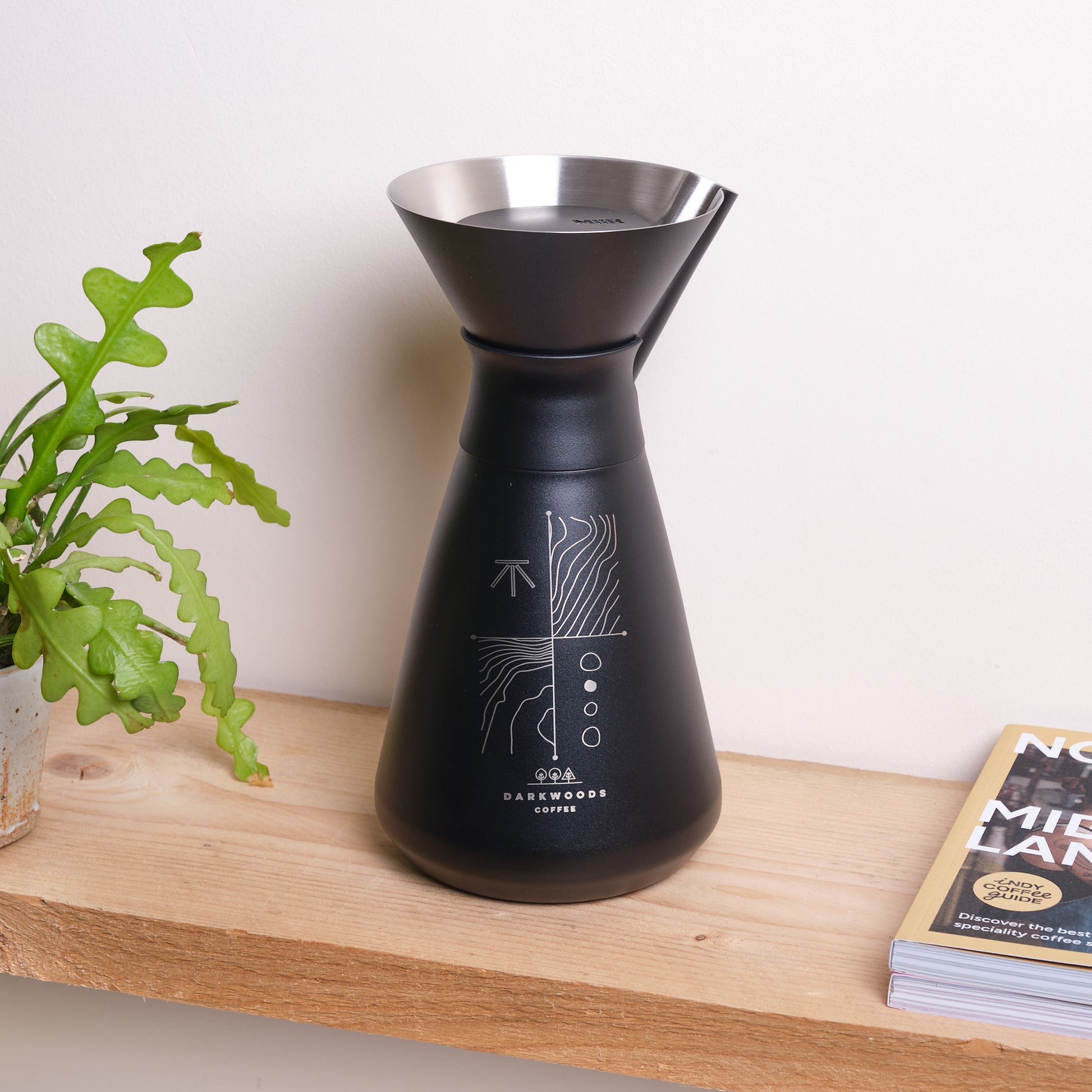 Black coffee brewing device on a wooden surface with a plant and book in the background